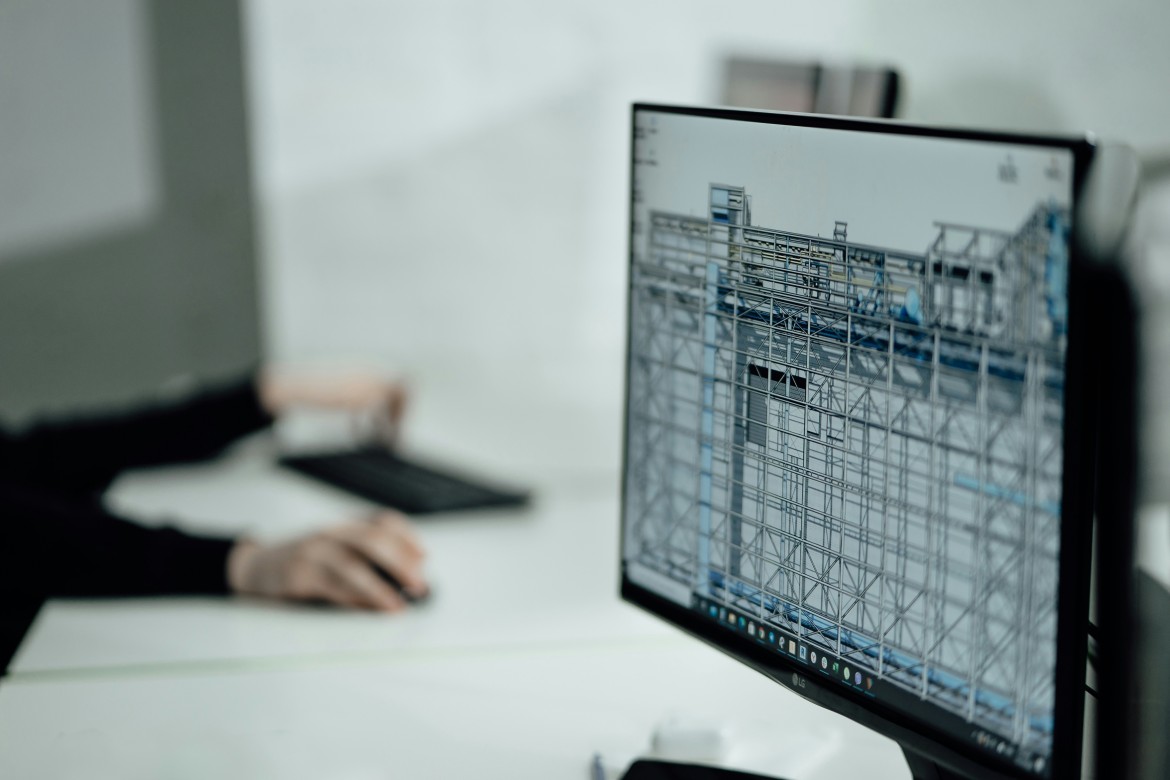 erson working at a desk using a computer displaying a detailed wireframe model of a building structure