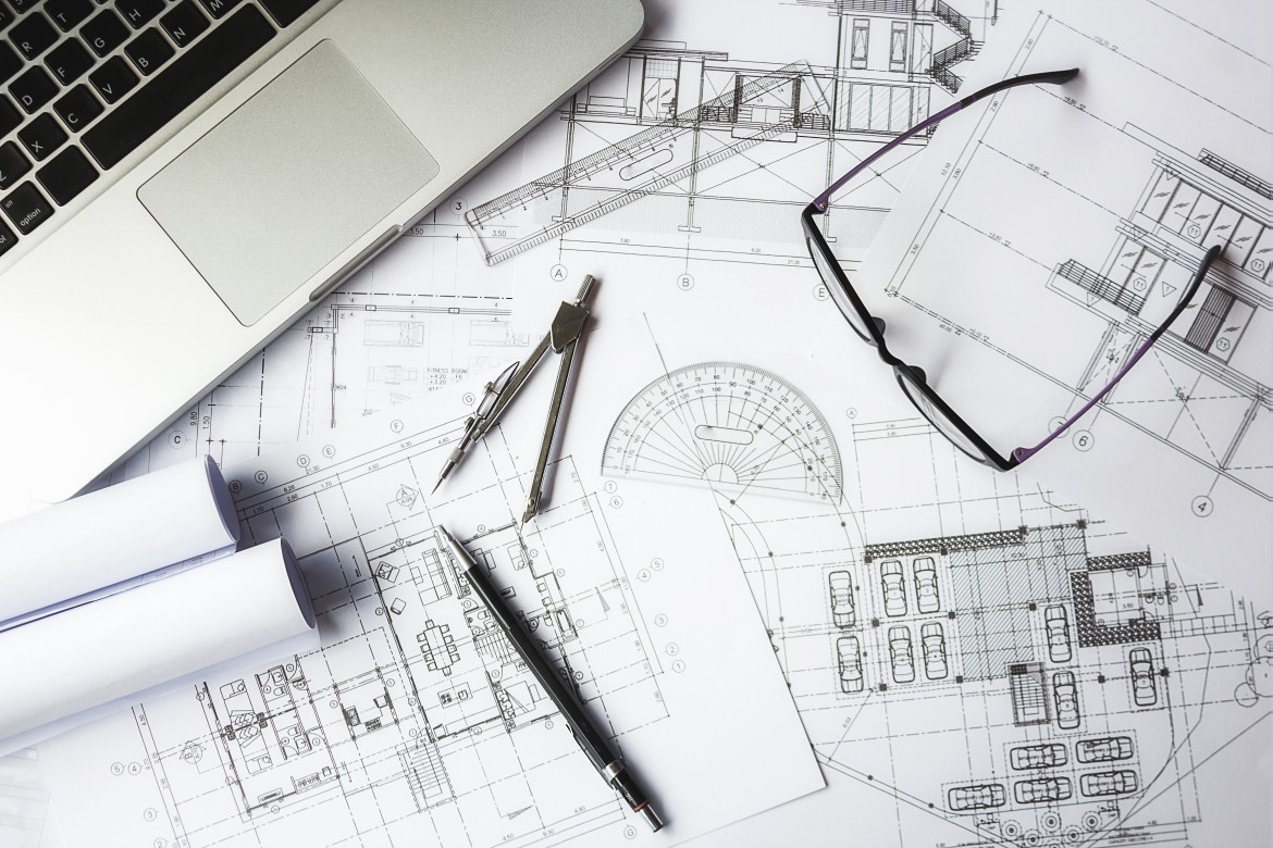 Architectural blueprints with laptop, drawing tools, and glasses on an engineer’s desk.
