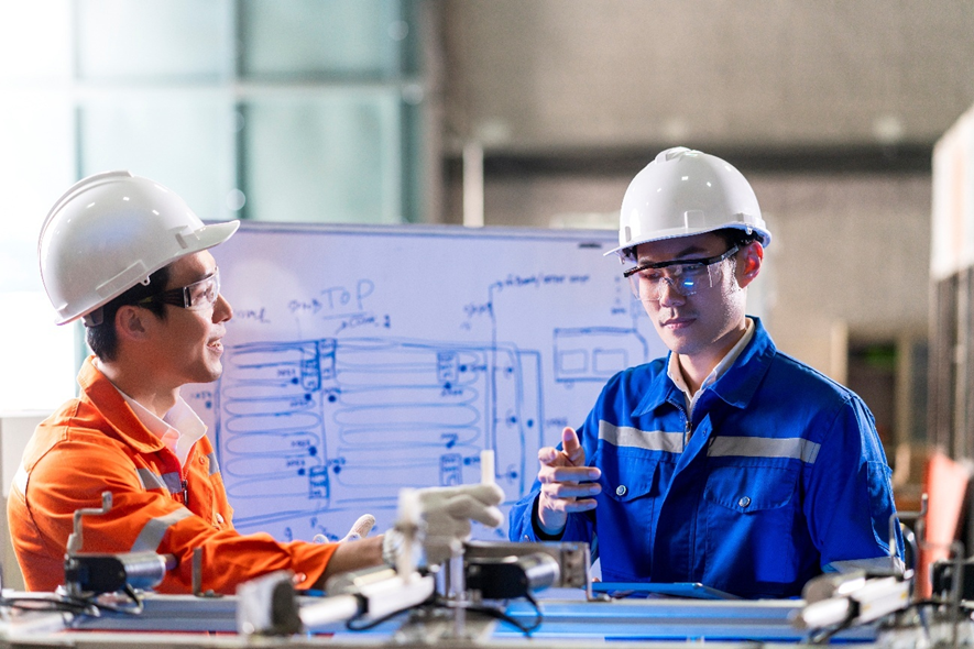 Two MEP engineers discussing system design plans in front of a whiteboard during a construction coordination meeting.