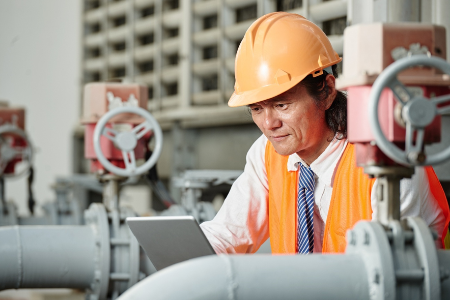 MEP engineer inspecting industrial piping system with a tablet during an on-site assessment.